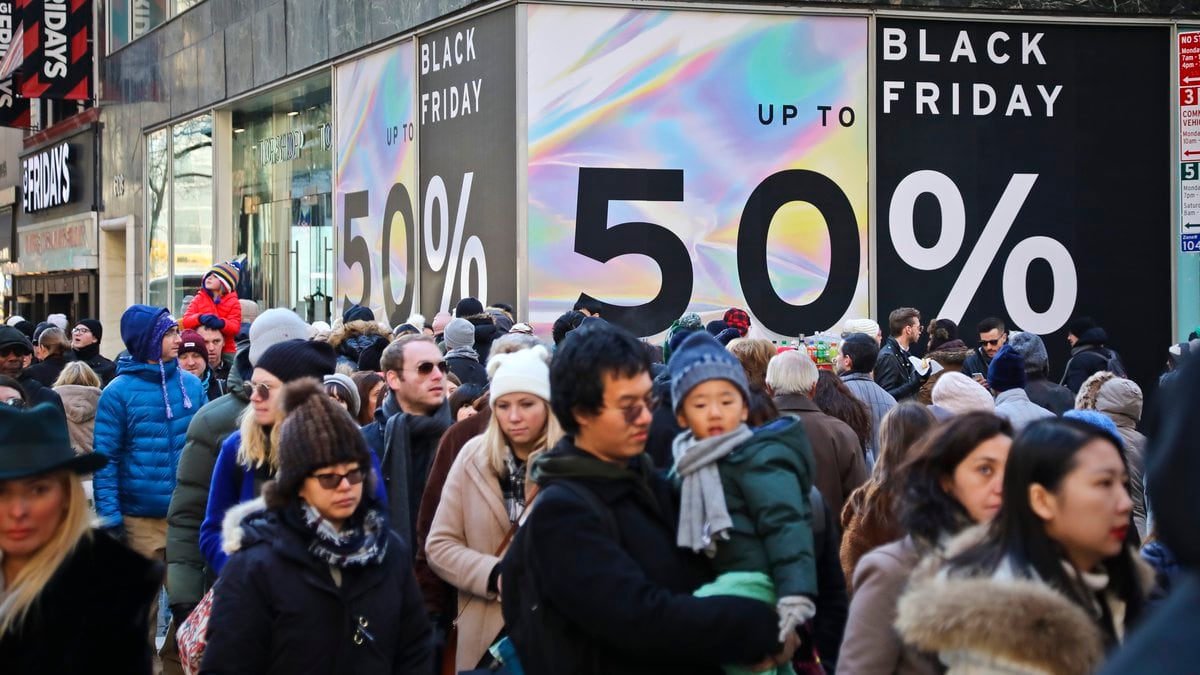 File - Crowds walk past a large store sign displaying a Black Friday discount in midtown...