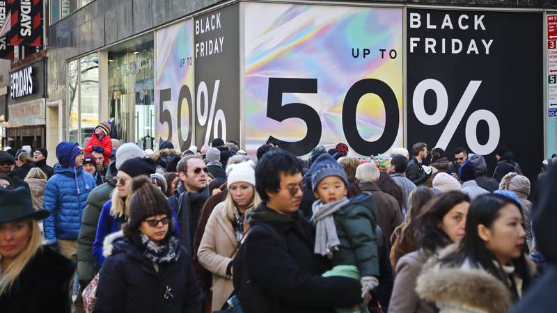 File - Crowds walk past a large store sign displaying a Black Friday discount in midtown...